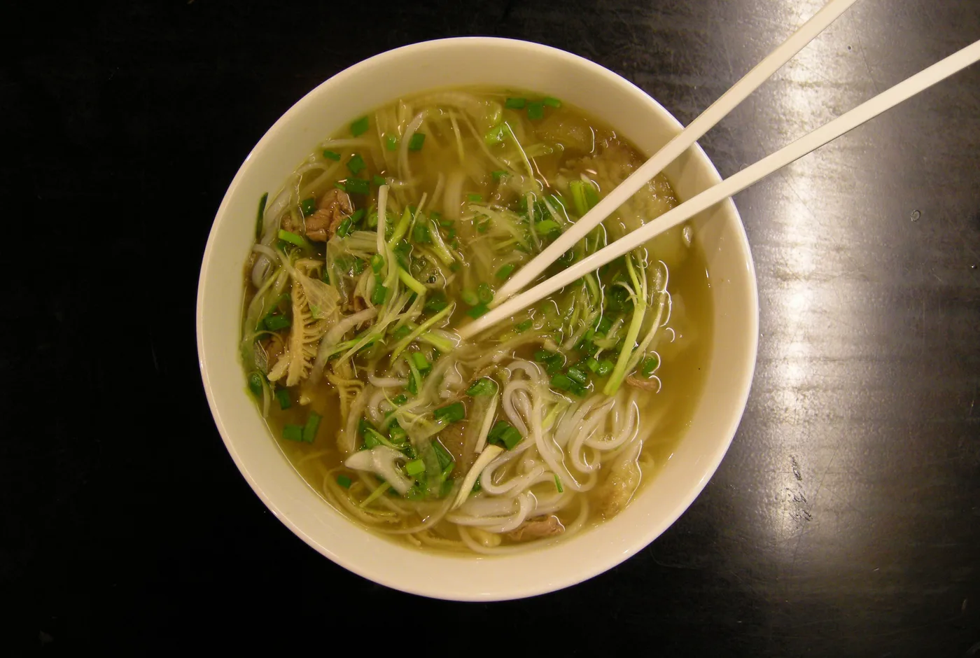 Schale Pho mit Reisbandnudeln, Rindfleisch, Lauchzwiebeln und Kräutern, dazu Stäbchen