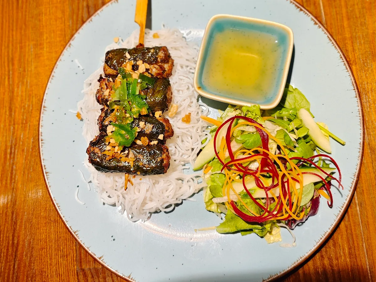 Reisnudeln mit gegrilltem Hack in Betelblättern, Salat und Dip auf einem hellen Teller