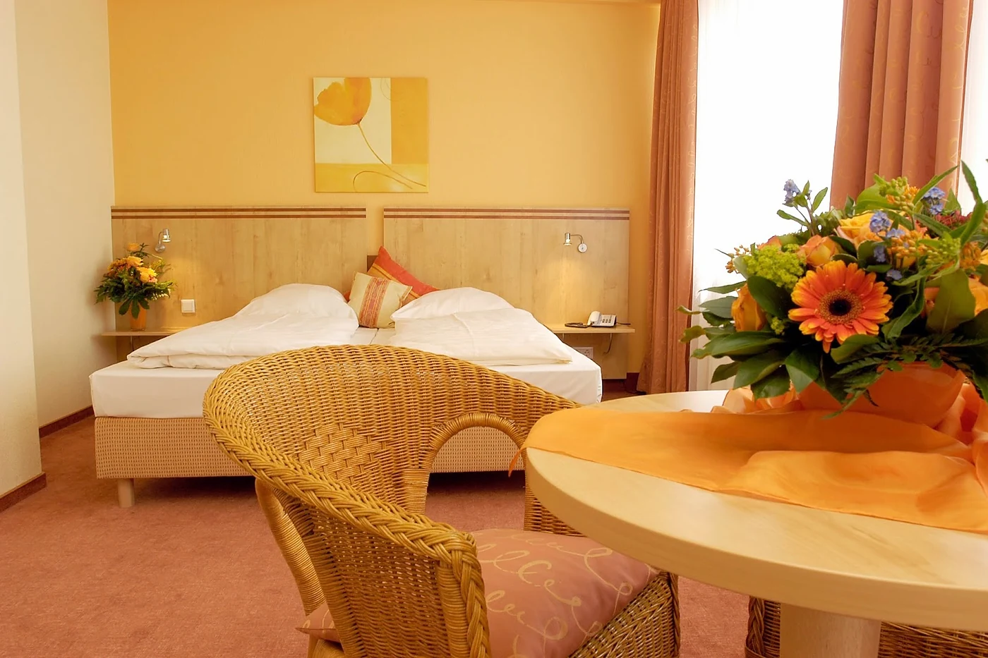 Zimmer mit Doppelbett, Korbstuhl und Blumenstrauß