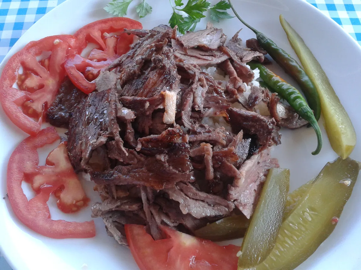 Dönerfleisch vom Drehspieß auf Reis mit Tomatenscheiben, Peperoni und eingelegten Gurken