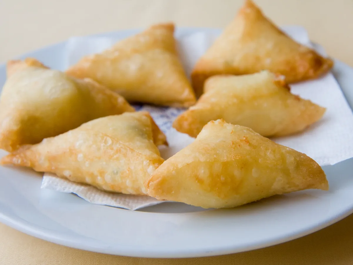 Fünf goldbraun frittierte Börek-Dreiecke auf einem hellen Teller
