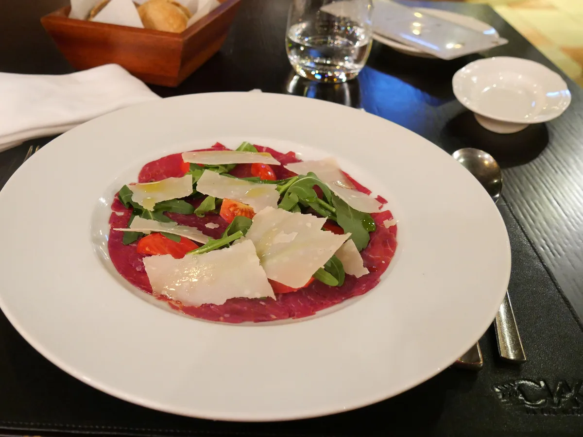 Rindercarpaccio mit Rucola, Kirschtomaten und Parmesanspänen auf einem weißen Teller