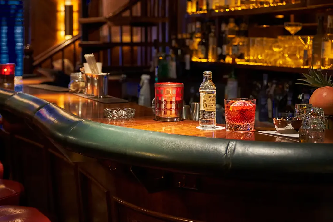 Gewölbter Tresen der Jahreszeiten Bar mit grünem Lederrand, Drink, Tonicflasche und Kerze vor der Flaschenwand