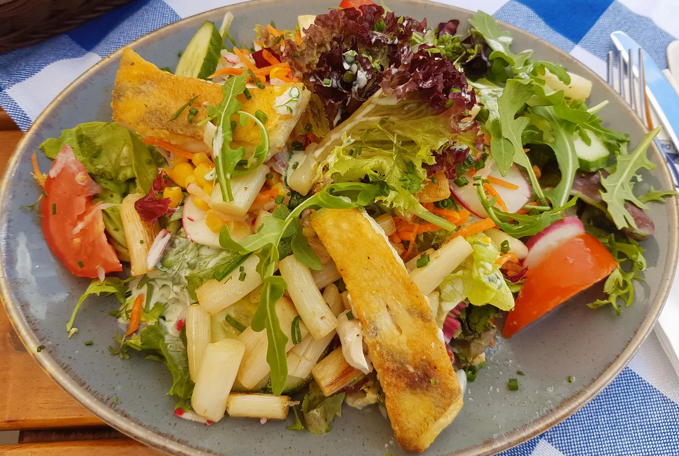 Gebratenes Zanderfilet mit weißem Spargel, Rucola und Blattsalat auf einem grauen Teller