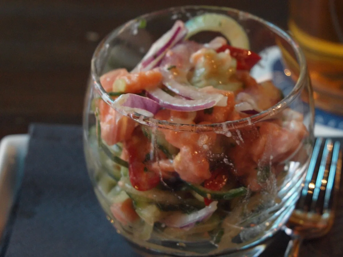 Roher Lachs mit roten Zwiebeln, Gurke und Tomate in einem Glas angerichtet