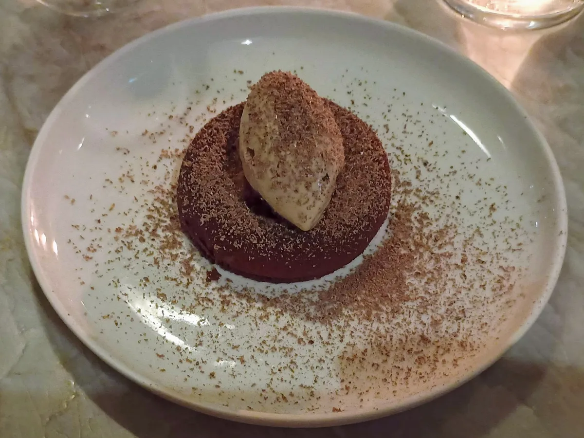 Schokoladendessert mit Kakaopulver und einer Nocke Eis auf einem hellen Teller