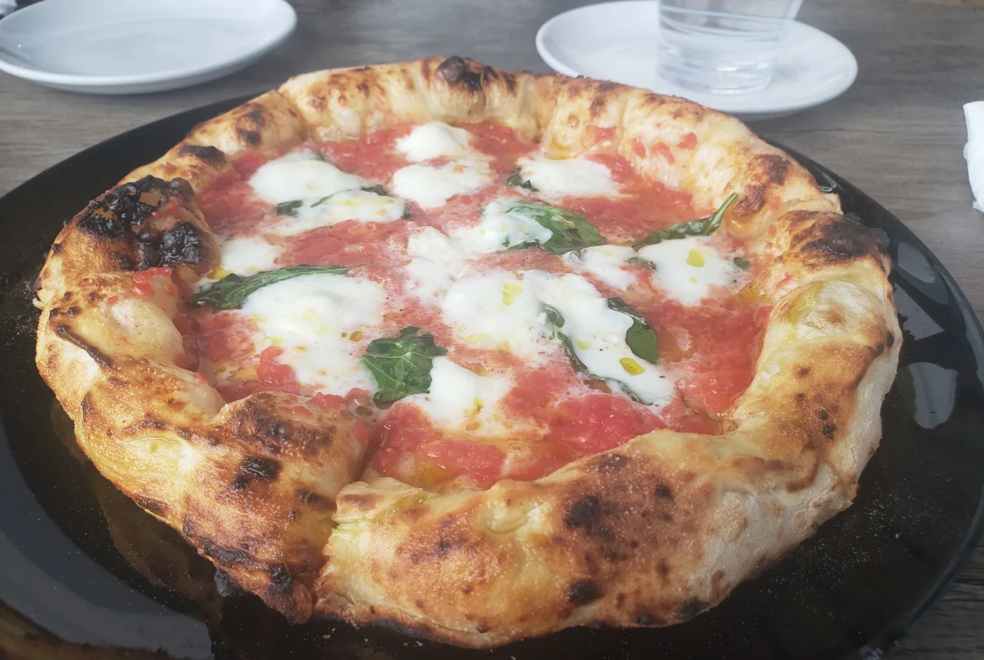 Neapolitanische Margherita mit hohem Rand, Tomaten und Mozzarella auf einem schwarzen Teller