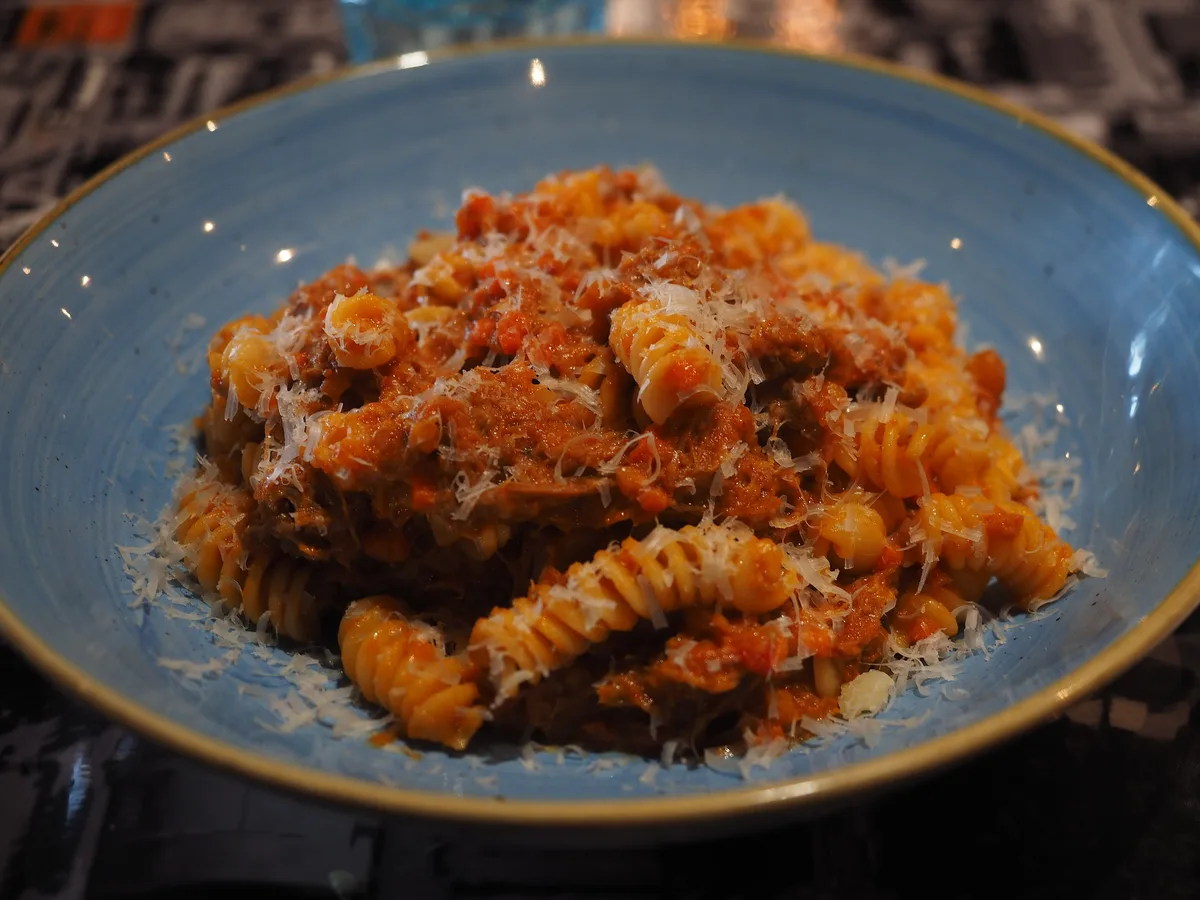 Fusilli mit Ragout und geriebenem Parmesan in einem blauen Teller
