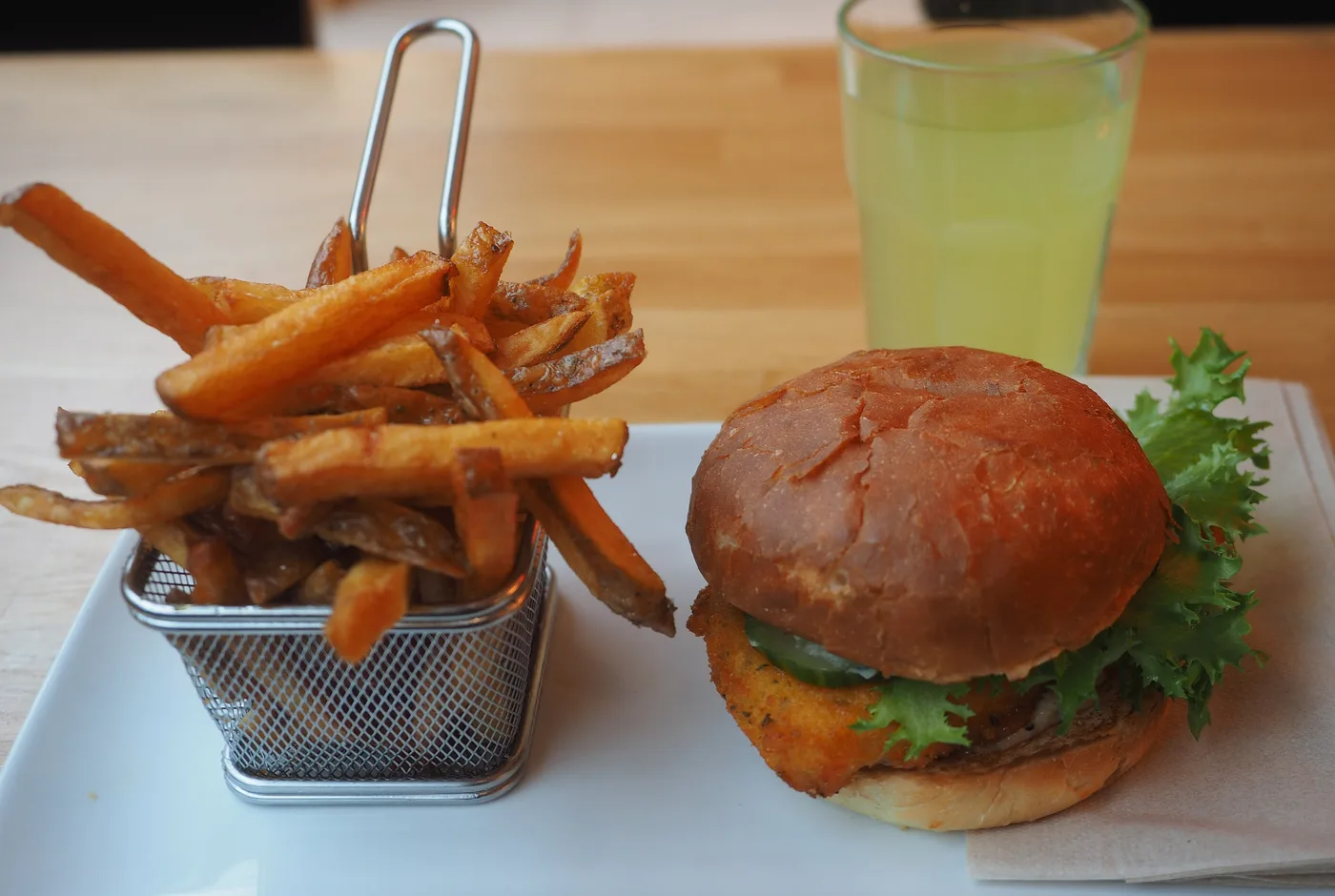 Burger im Brioche-Brötchen mit Salat, daneben Pommes frites in einem Drahtkörbchen