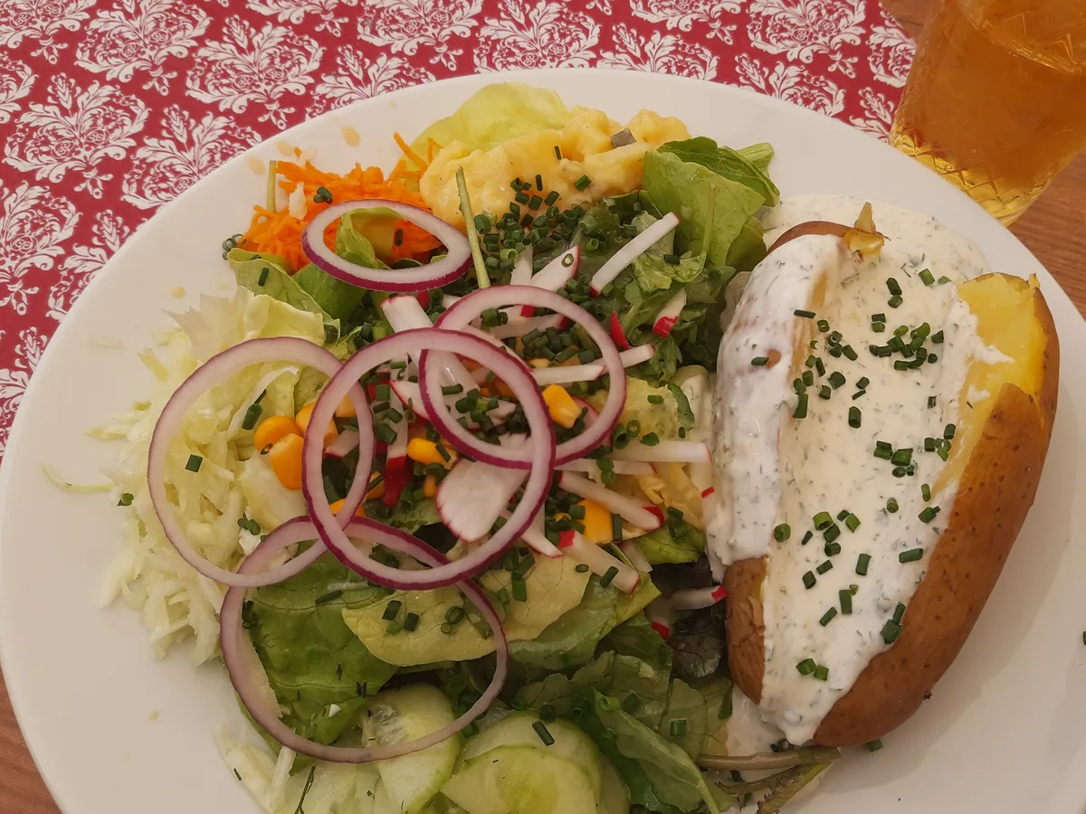 Ofenkartoffel mit Kräuterquark und Schnittlauch, daneben gemischter Salat auf einem weißen Teller