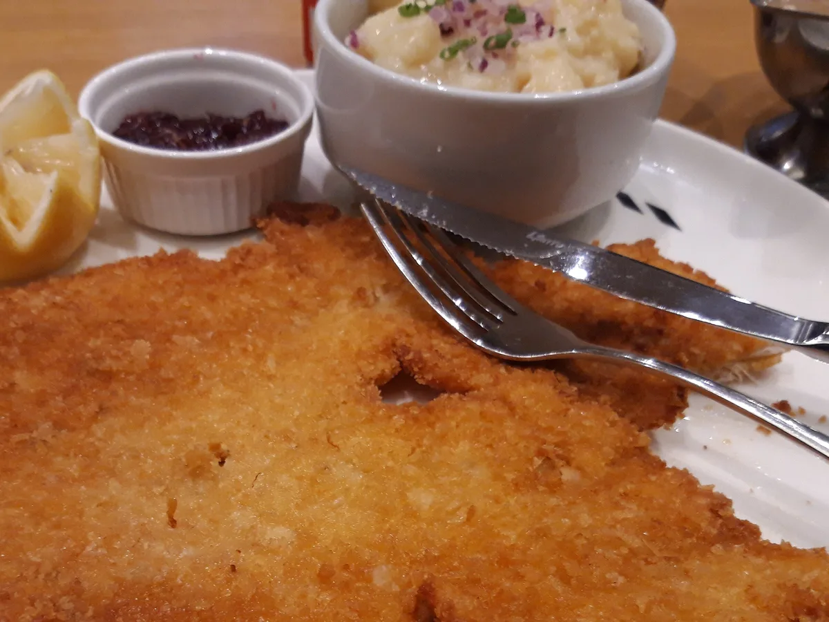 Knusprig paniertes Hähnchenschnitzel auf einem weißen Teller, daneben Zitrone und Kartoffelsalat