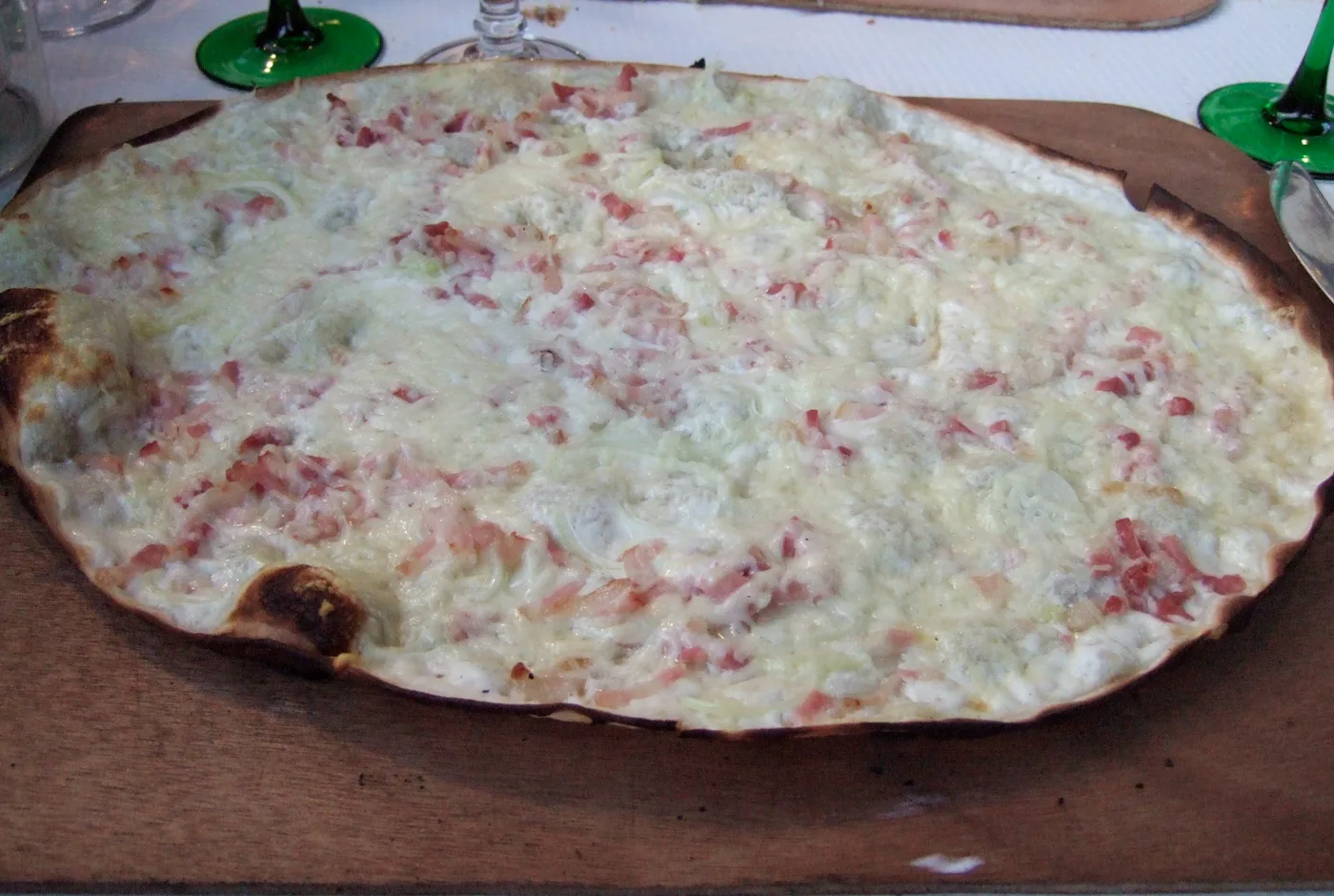 Dünner Flammkuchen mit Speckwürfeln, Zwiebeln und Sahne auf einem Holzbrett