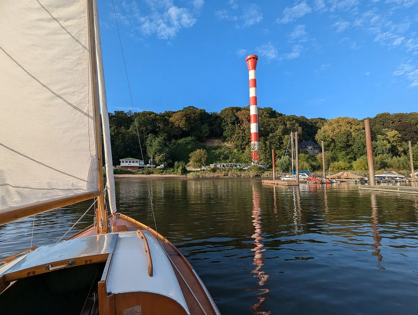 Blick von einem hölzernen Jollenkreuzer auf den Jollenhafen mit rotweißem Leuchtturm
