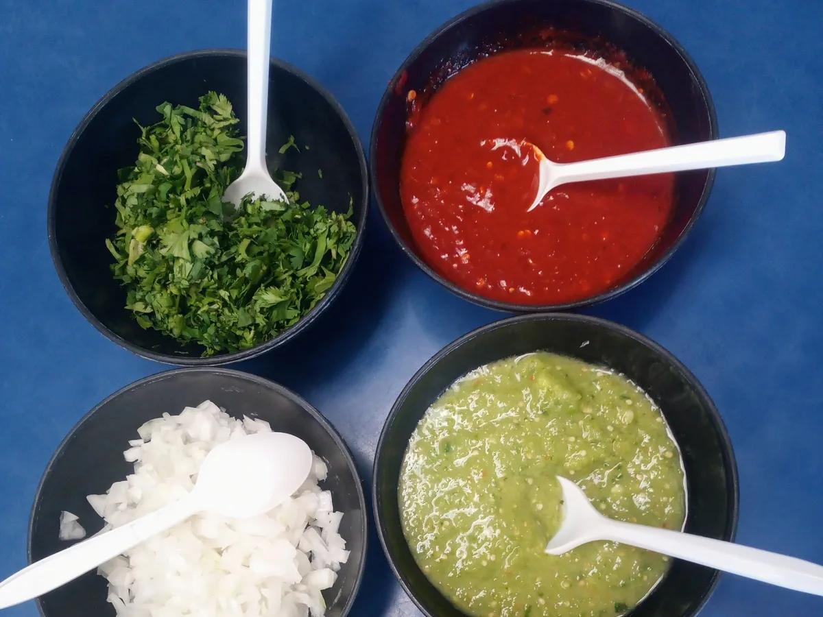 Schalen mit roter und grüner Salsa, gehacktem Koriander, Zwiebeln und Limetten