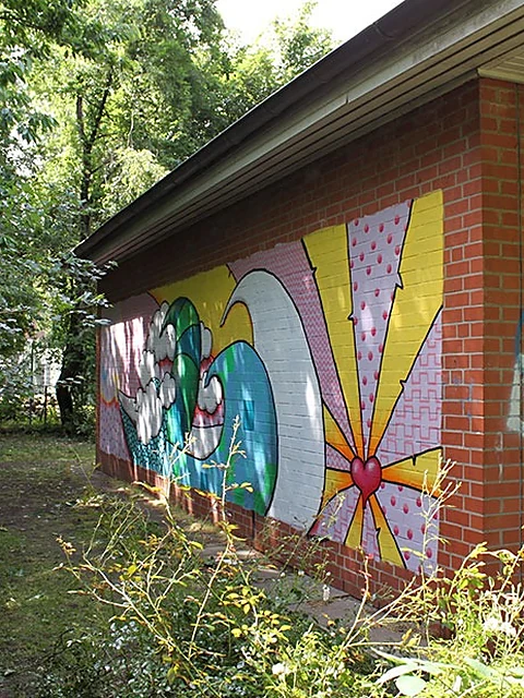 Buntes Graffiti mit Wellen, Sonnenstrahlen und Herz an der Backsteinwand des Jugendcafés, davor Büsche