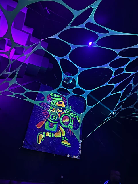 Türkis leuchtendes Netz unter der Clubdecke mit Discokugel und einem bemalten Neonbanner