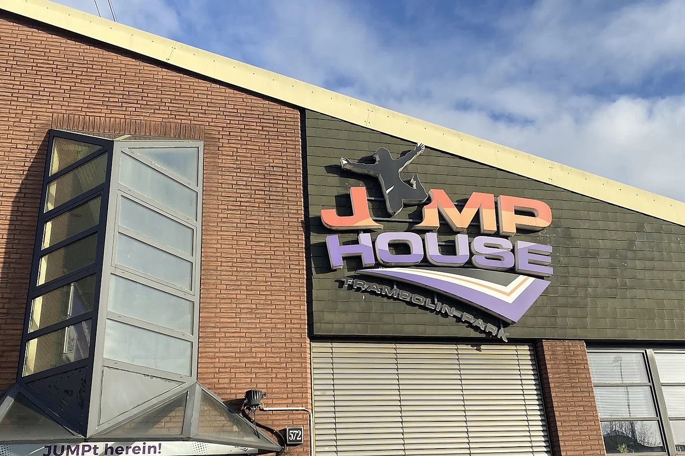 Backsteinfassade mit großem Leuchtschriftzug JUMP HOUSE Trampolin-Park über dem Eingang, daneben der Schriftzug JUMPt he