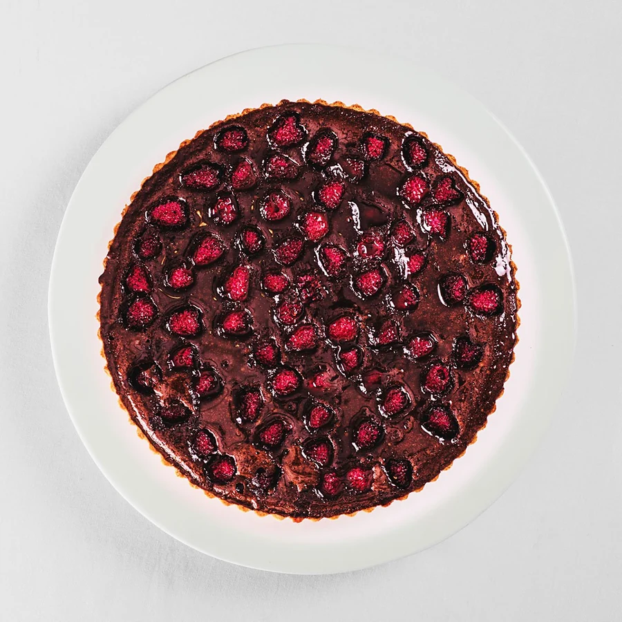 Ganze Himbeer-Schokoladen-Tarte von oben auf weißem Teller