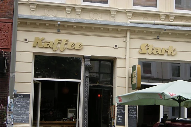Fassade des Kaffee Stark mit goldenem Schriftzug, Kreidetafeln neben der Tür und grünem Sonnenschirm