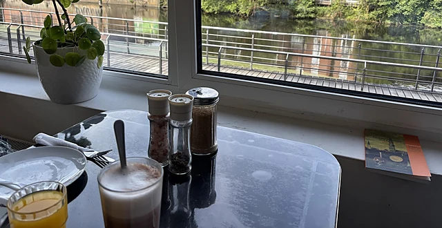 Latte Macchiato und Gewürzstreuer auf einem Tisch am Fenster mit Blick auf den Veringkanal und rote Backsteinhäuser