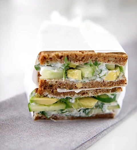 Doppelt belegte Vollkornstulle mit Frischkäse, Avocado und Gurke, in Papier eingeschlagen