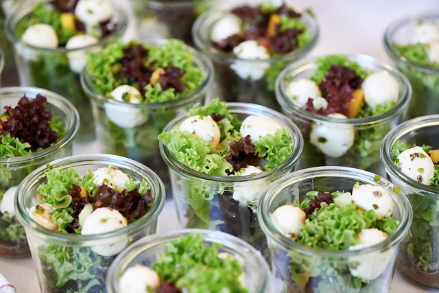 Viele kleine Gläser mit Salat, Mozzarella-Kugeln und Tomaten auf einem Tablett