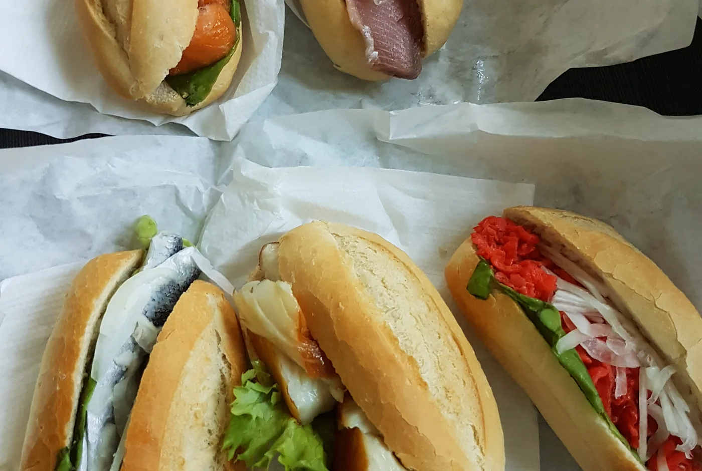 Mehrere Fischbrötchen mit Matjes, Lachs, Backfisch und Zwiebeln auf Papier