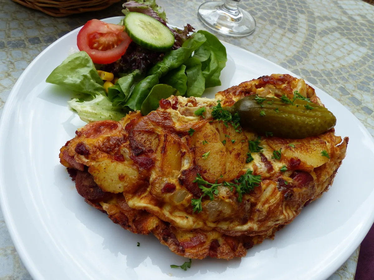 Bauernfrühstück aus Bratkartoffeln, Ei und Speck mit Salatbeilage und Gewürzgurke
