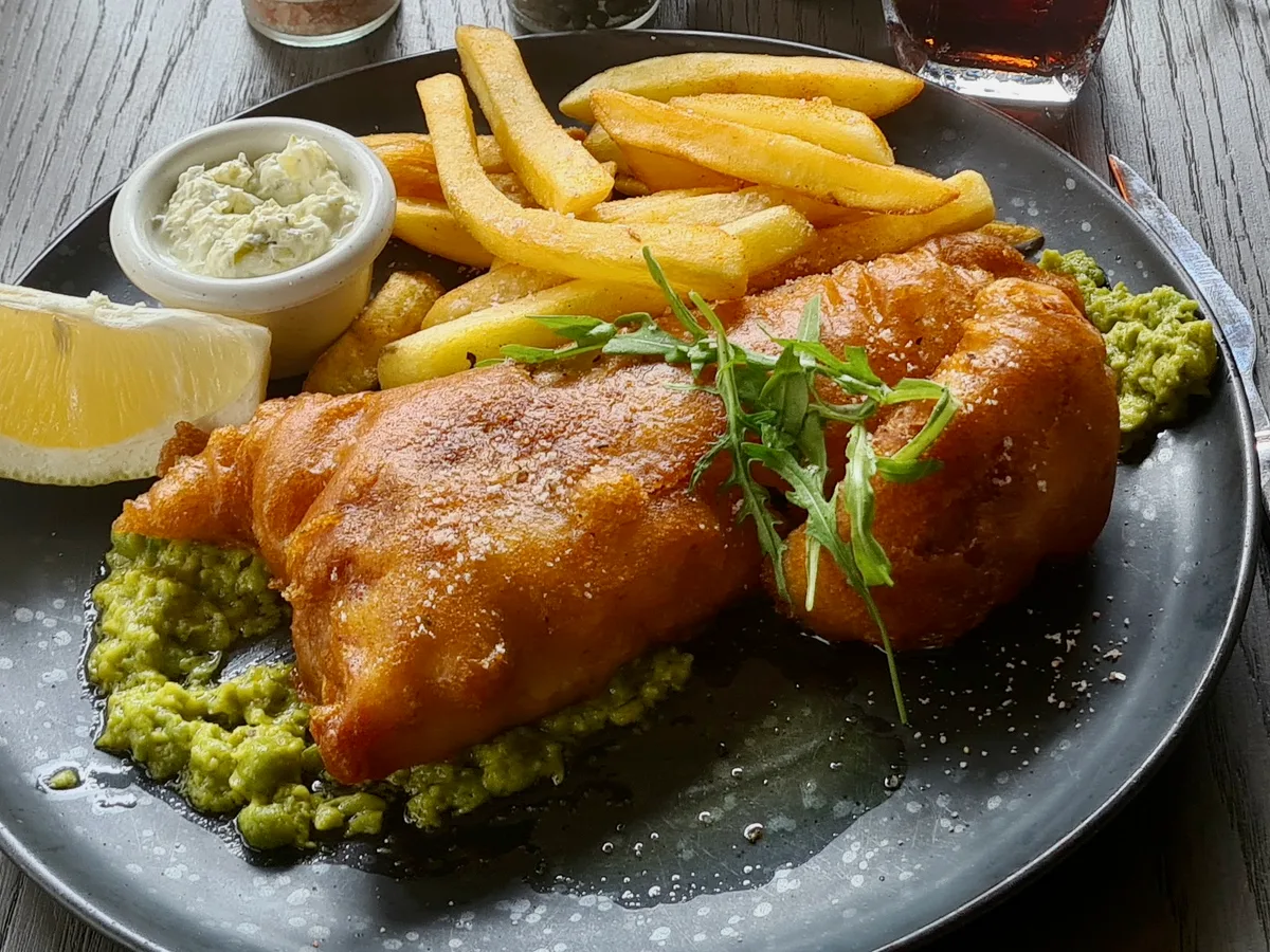 Im Bierteig gebackenes Fischfilet mit Pommes, Zitrone und Remoulade auf einem grauen Teller