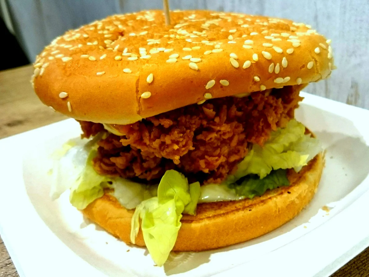 Chicken Burger mit paniertem Hähnchenfilet, Salat und Sesambrötchen auf einem weißen Teller