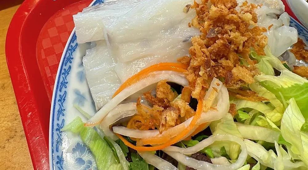 Bánh cuốn, gedämpfte Reisrollen mit Röstzwiebeln, Möhren und Salat auf blau-weißem Teller
