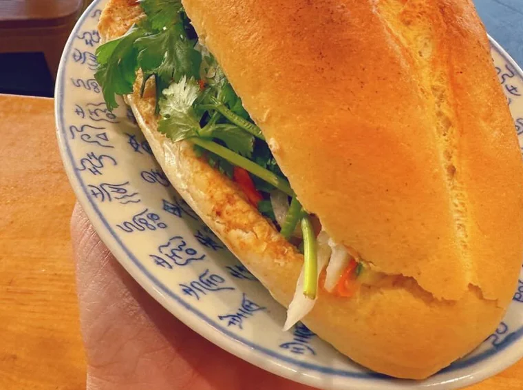 Nahaufnahme eines Bánh mì mit Koriander, Gurke, eingelegten Möhren und Chili im knusprigen Baguette