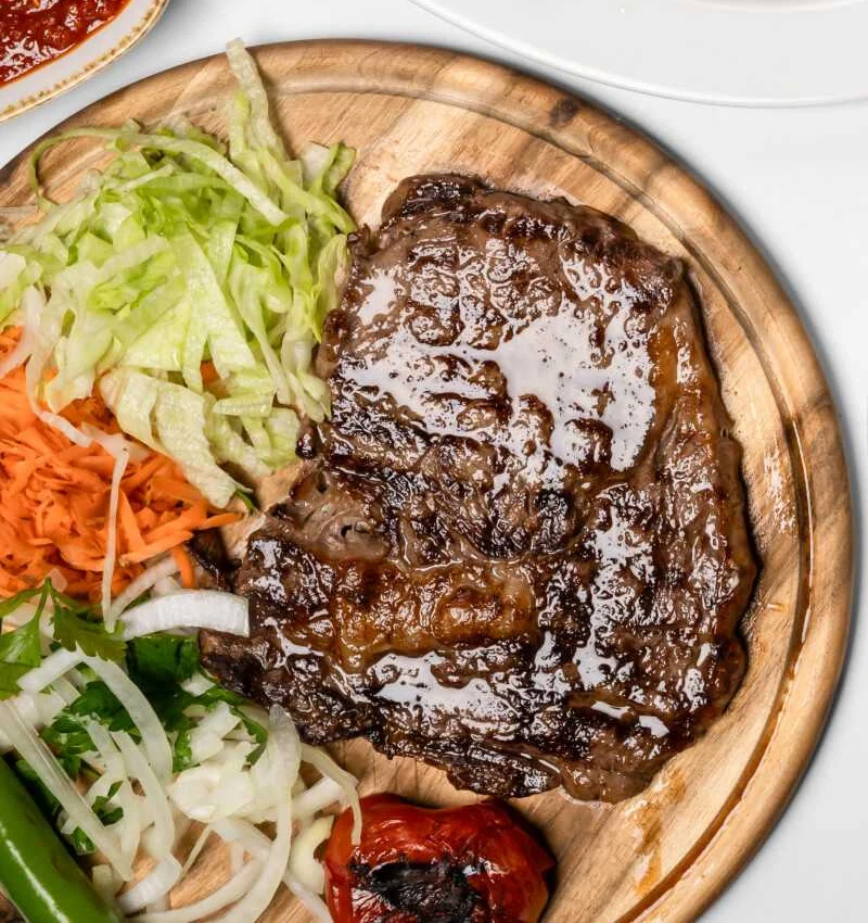 Gegrilltes Steak auf Holzbrett mit Salat, gegrillter Tomate und grüner Peperoni