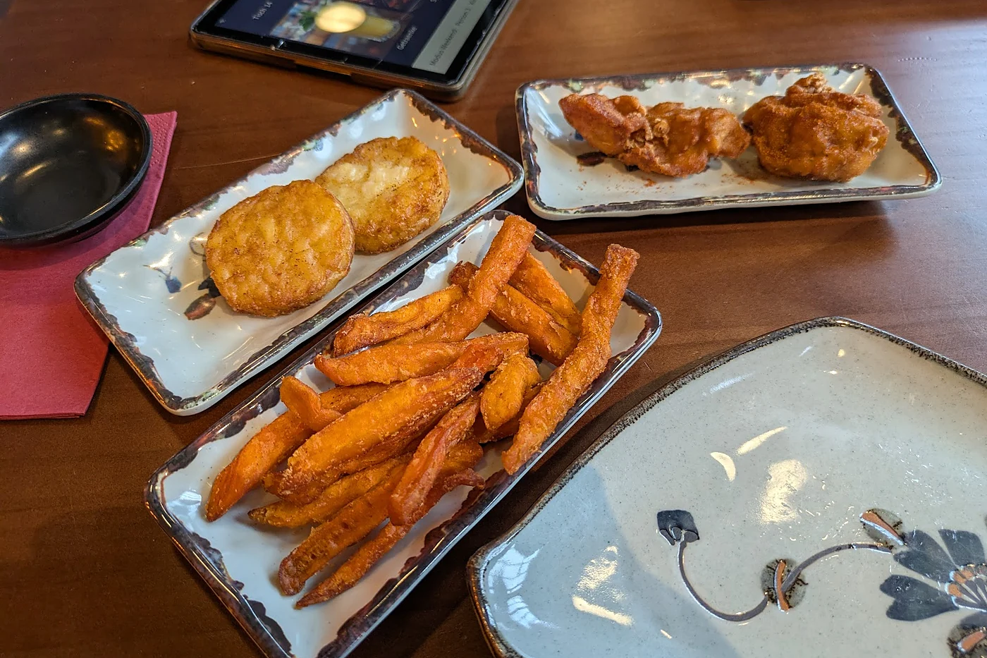 Mehrere Teller mit Süßkartoffelpommes und Frittiertem auf dem Tisch, daneben das Bestell-Tablet