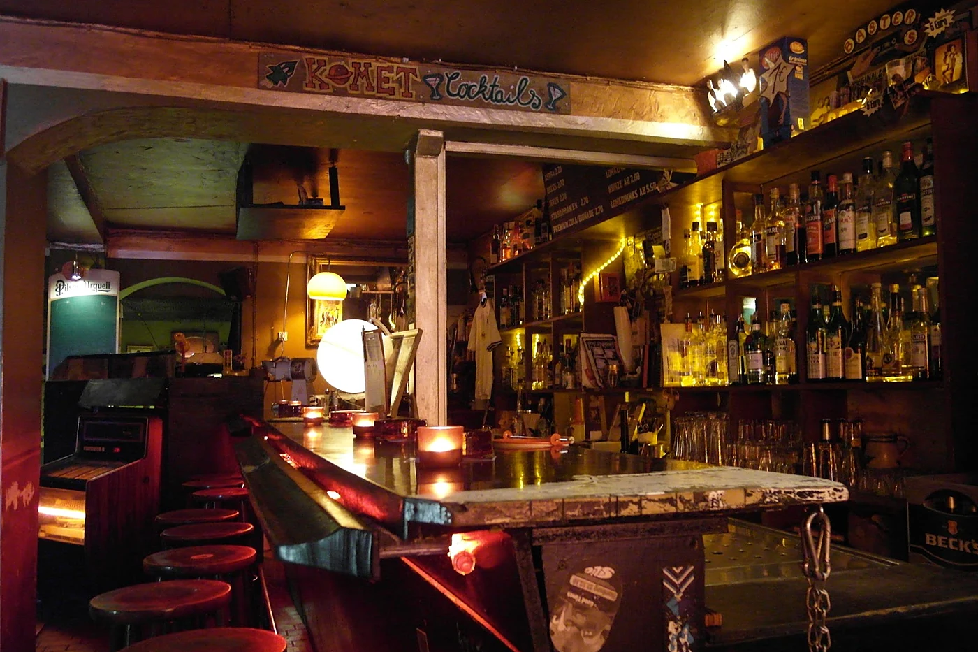Tresen der Komet Musik Bar mit Barhockern, Flaschenregalen, Jukebox und dem gemalten Schriftzug Komet Cocktails