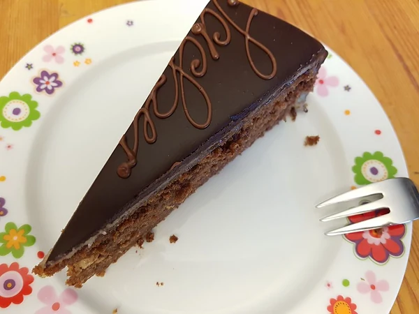 Stück Sachertorte mit Schokoladenglasur und Schriftzug auf einem Blümchenteller