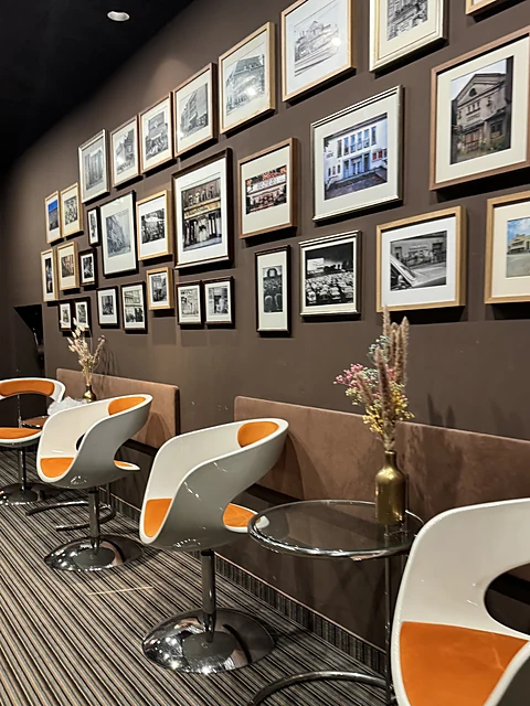 Wartebereich mit weiß-orangen Drehsesseln, Glastischen und einer Wand voller gerahmter Fotografien alter Kinogebäude