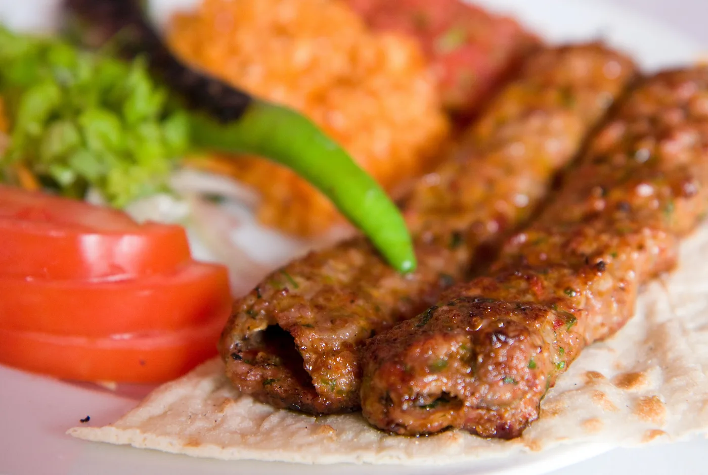 Zwei Adana-Kebap-Spieße auf Fladenbrot mit Tomate, Salat und Ezme