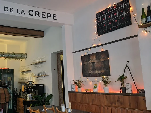 Gastraum der Crêperie mit Holztresen, Weinregal, Lichterkette und Bildern von Cidre-Fässern