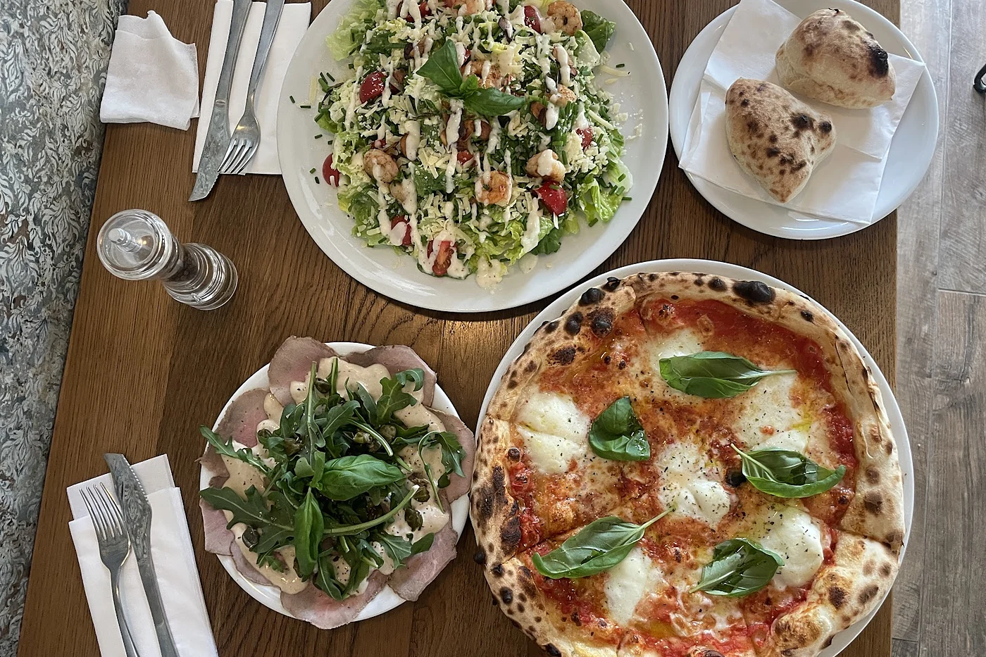 Zwei Pizzen und ein Salat auf einem Holztisch