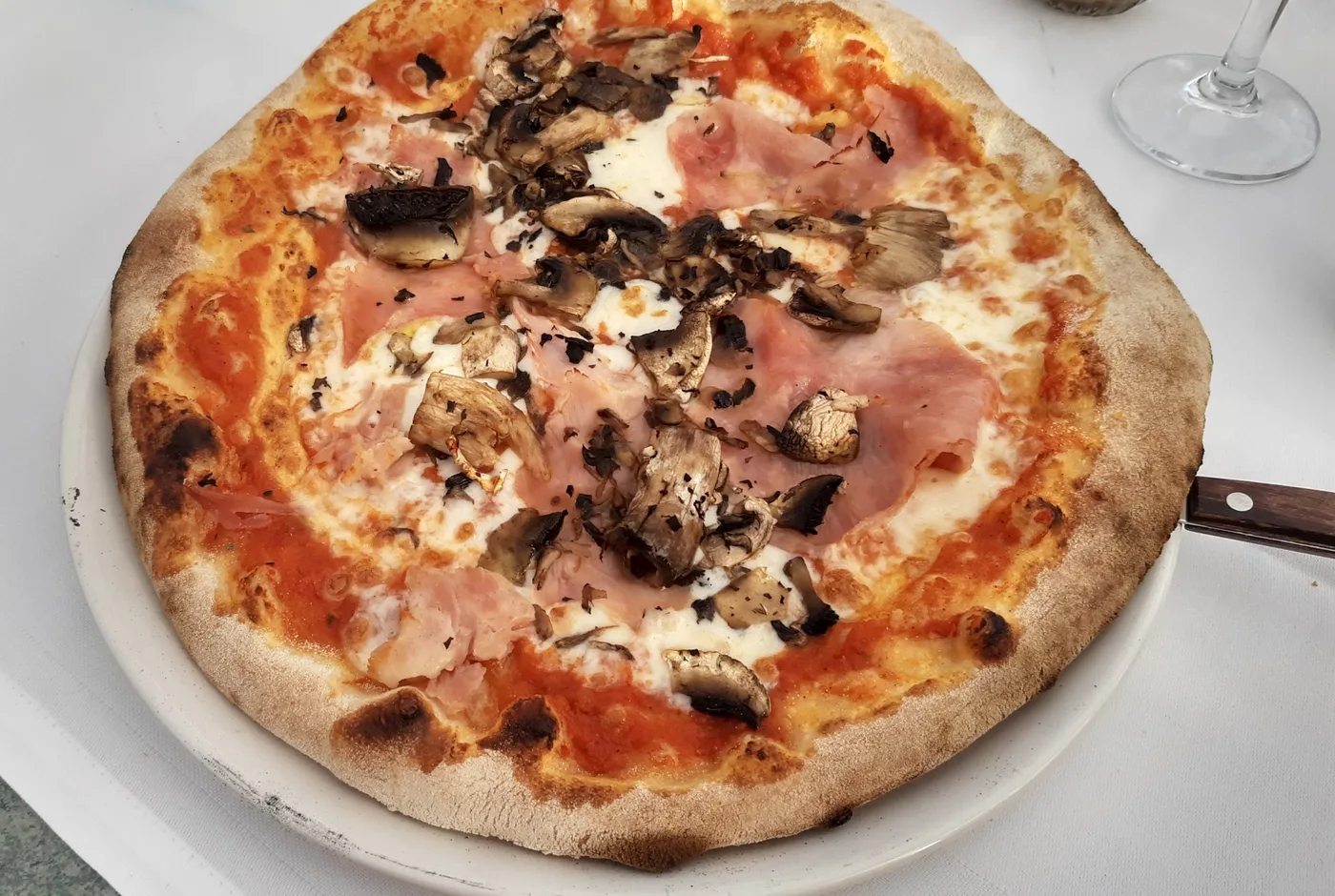 Pizza mit Schinken, Champignons und Mozzarella auf einem weißen Teller