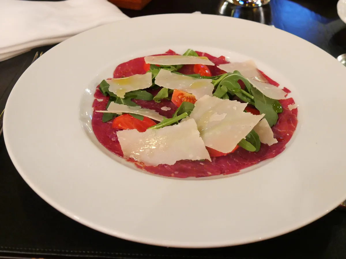 Carpaccio mit Rucola, Parmesanspänen und Kirschtomaten auf einem weißen Teller