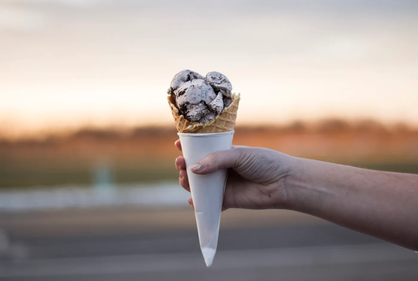 Eiswaffel mit mehreren Kugeln, in der Hand gehalten vor abendlichem Himmel