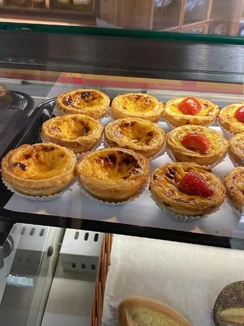 Pastéis de Nata, teils mit Erdbeere, auf einem Blech in der Vitrine