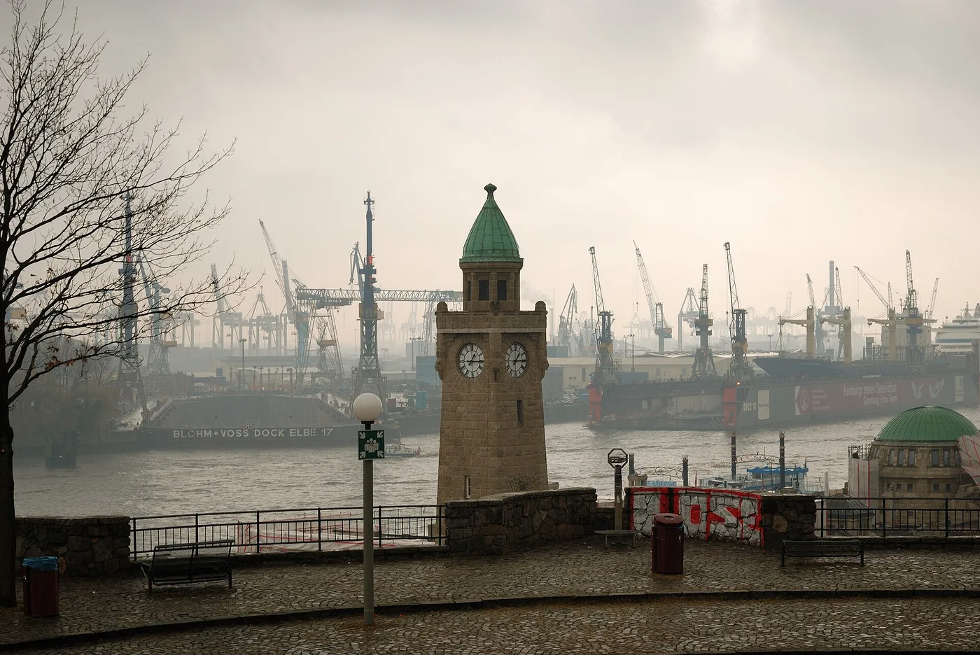 Pegelturm an den Landungsbrücken in Hamburg mit Hafenkränen im Nebel