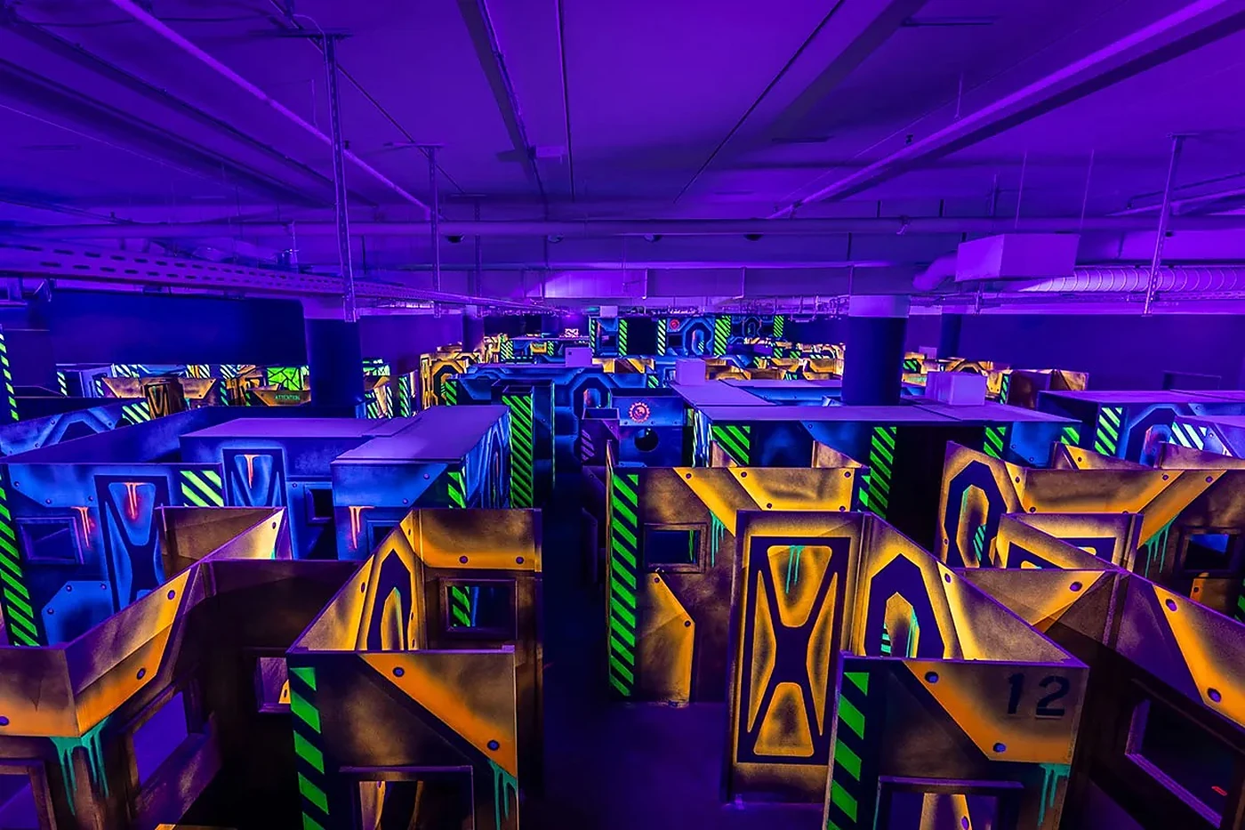 Lasertag-Arena im Schwarzlicht mit gelb-grün leuchtenden Deckungen und Wänden auf mehreren Ebenen