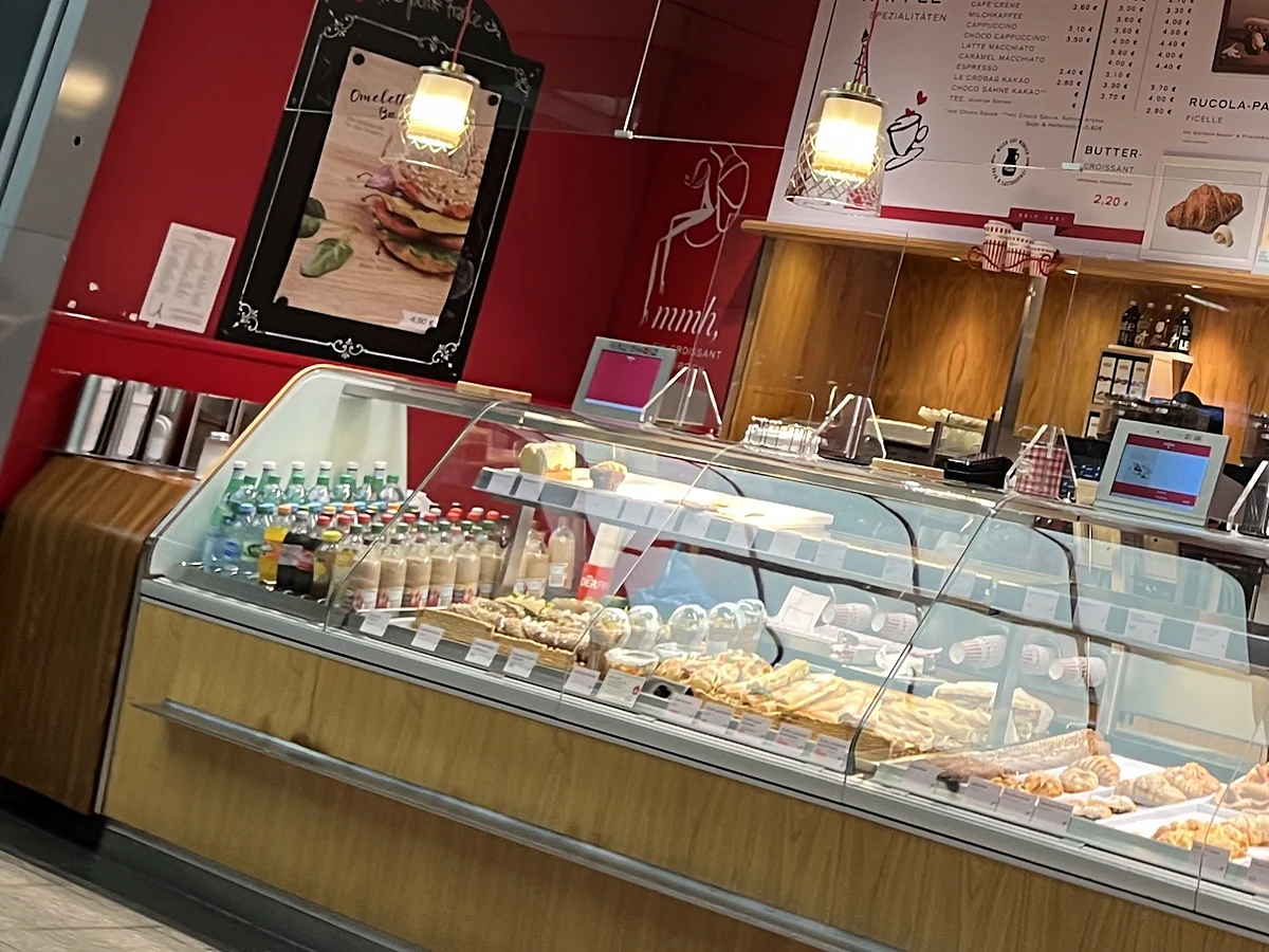 Theke mit Glasvitrine voller Baguettes und Gebäck, davor gekühlte Getränke