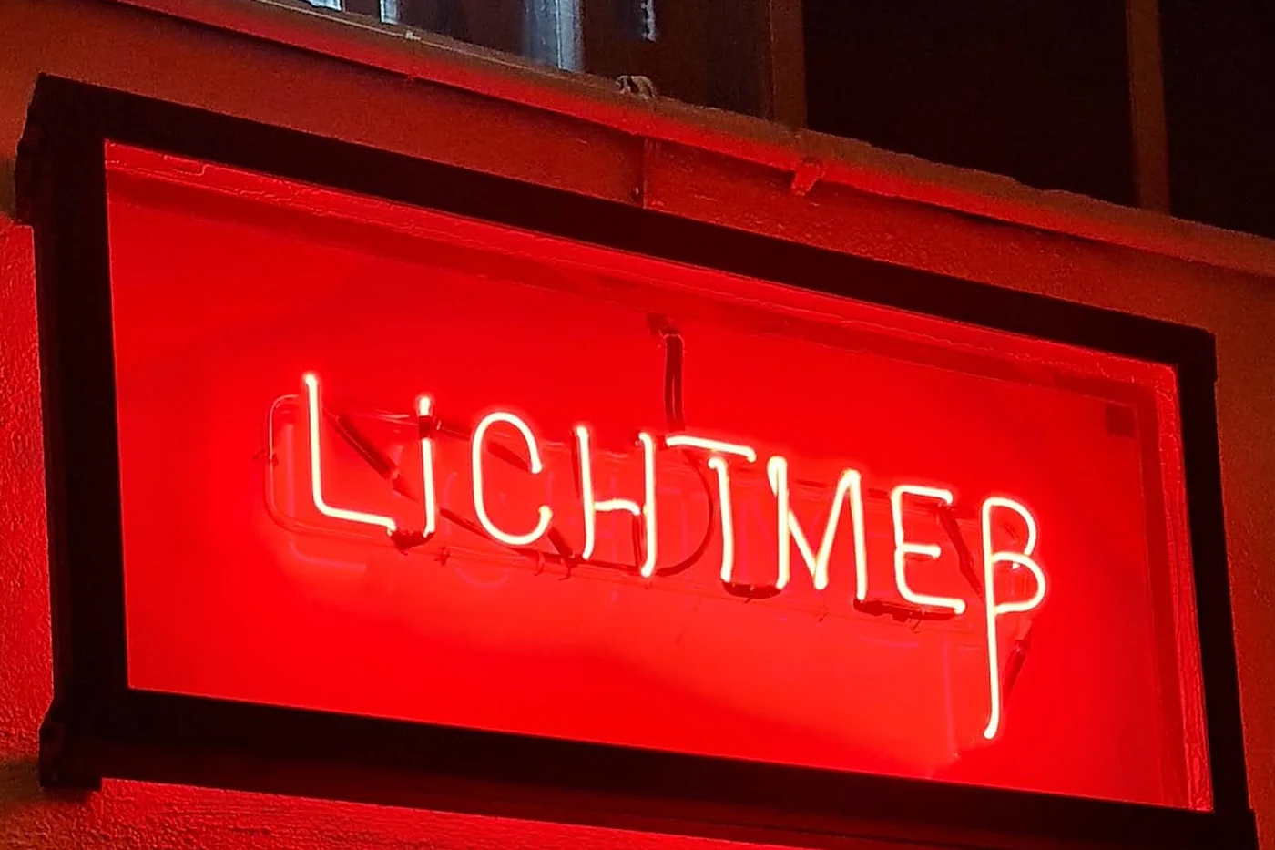 Rot leuchtendes Neonschild mit dem Schriftzug Lichtmeß in einem dunklen Metallrahmen an einer Wand