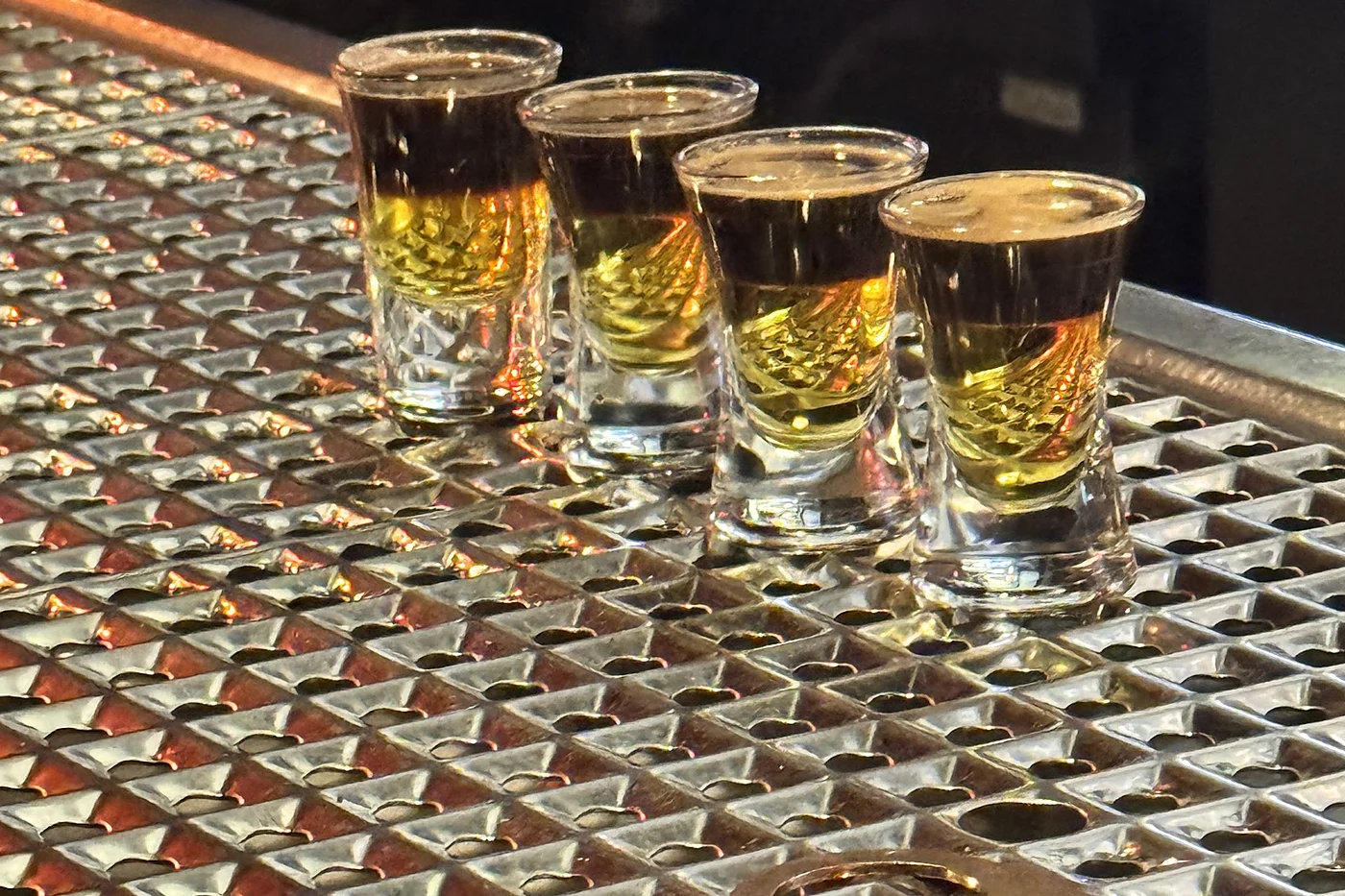 Vier Shotgläser mit goldbraunem Schnaps auf einer gerippten Kupfer-Tresenplatte