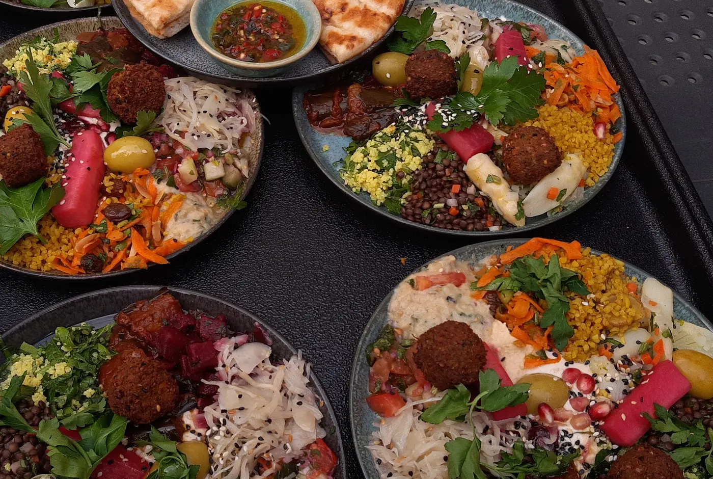 Mehrere Teller mit orientalischen Vorspeisen, Falafel, Linsen, Bulgur, Salaten und eingelegtem Gemüse auf einem Tablett
